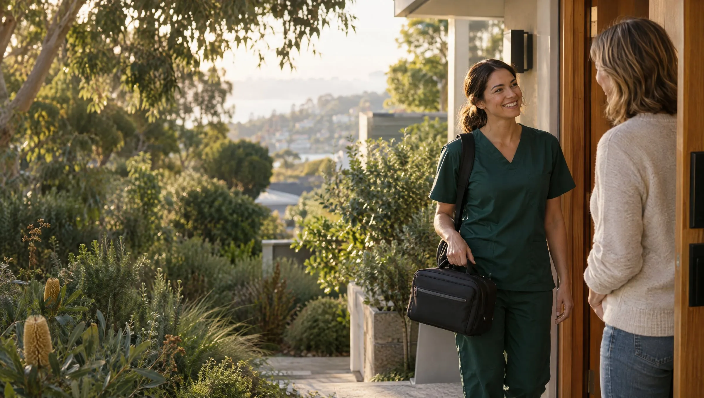 An Express nurse in green scrubs smiling as she is welcomed at a patient's front door in the morning sun
